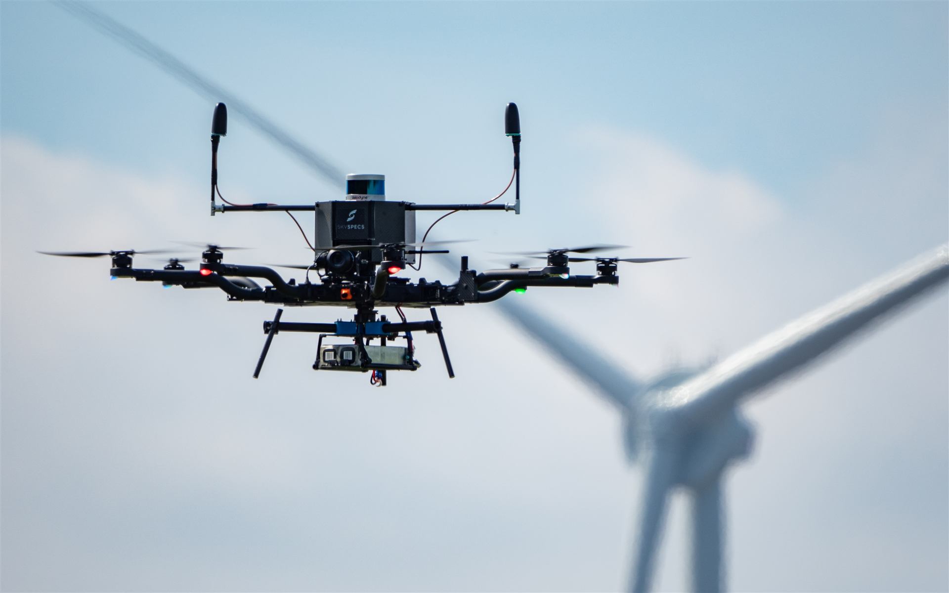 SkySpecs inspection drone in flight with a wind turbine rotor behind it