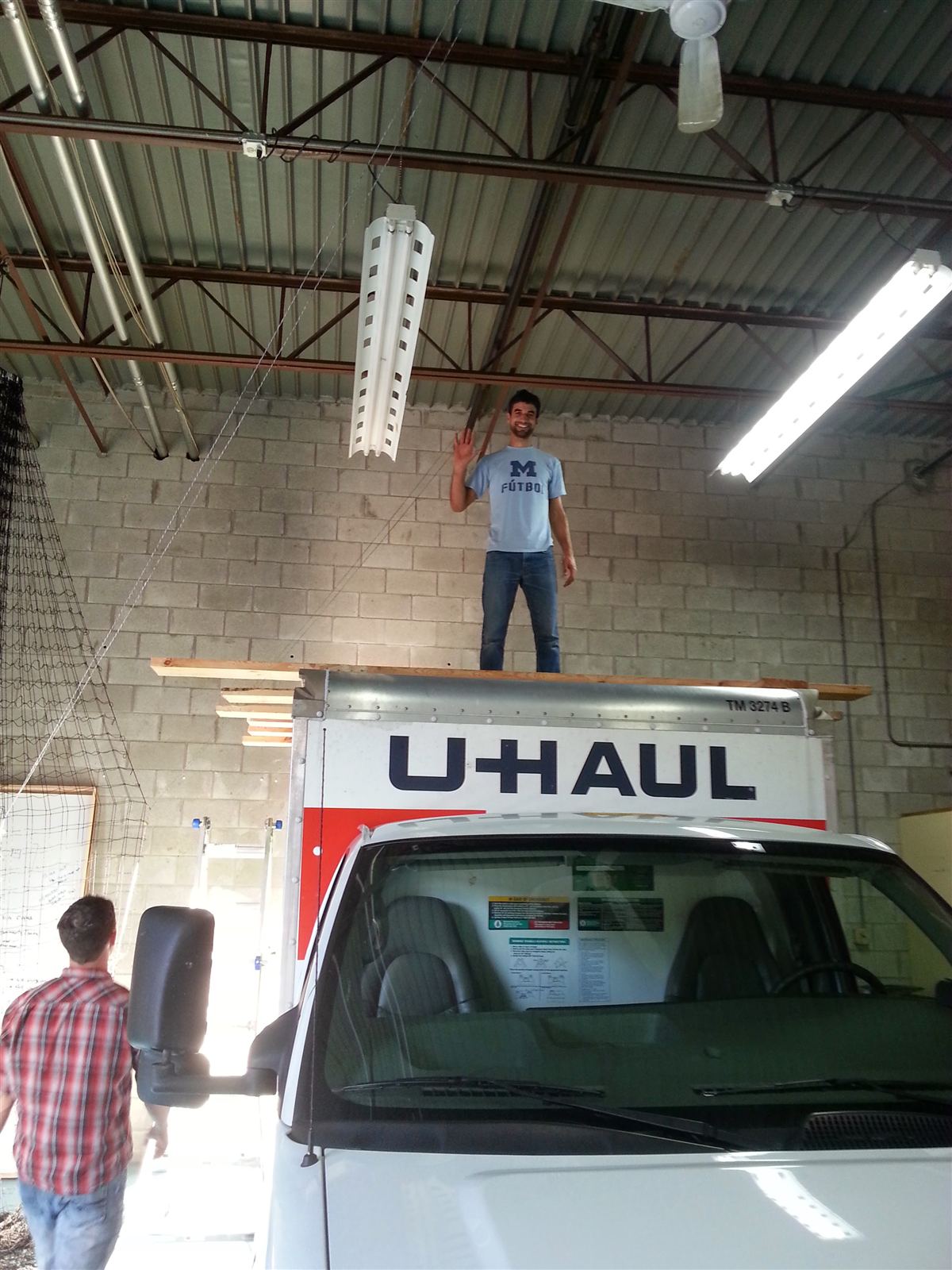 SkySpecs co-founder standing on planks laid across the roof of a U-Haul truck inside the first warehouse office, rigging a drone-test net to the 20-foot ceiling